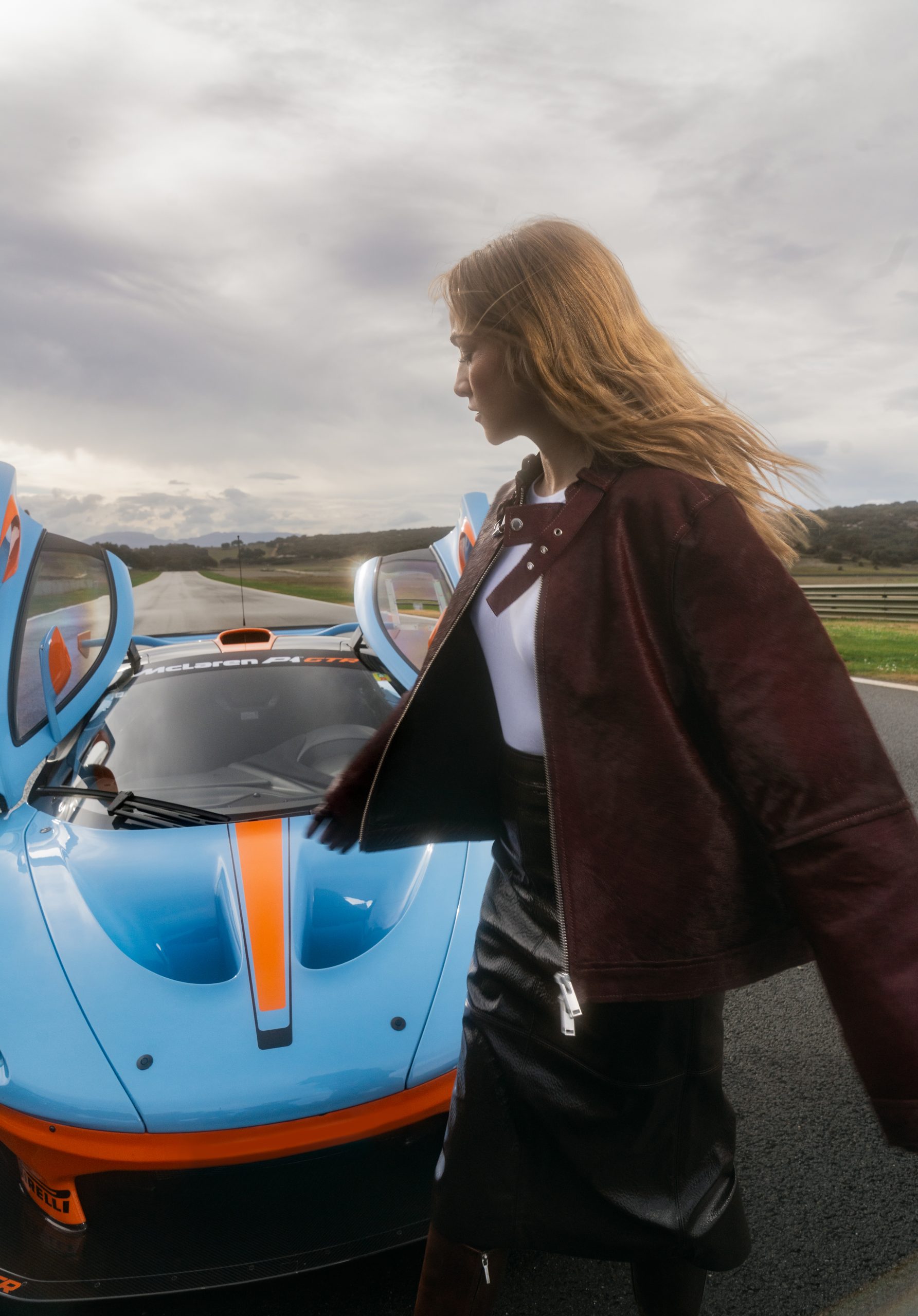 Carmen looking back at a supercar she is standing in front of