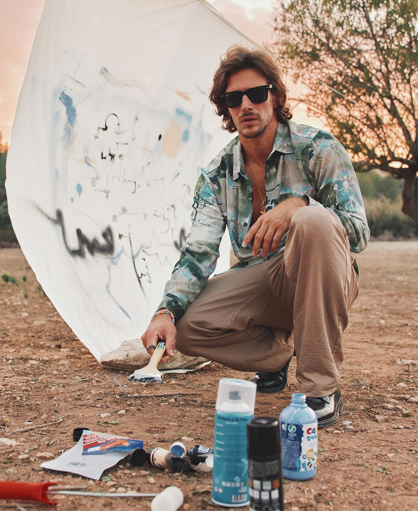 Jake crouched over his equipment outside with a painting in progress in the background