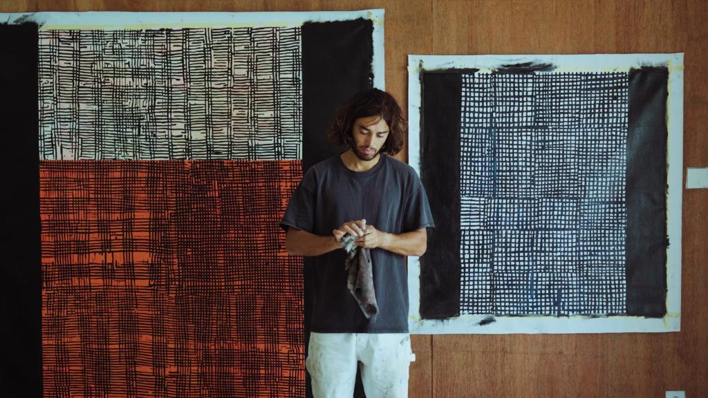 An image of Naleye holding a cloth in his hands standing in front of paintings