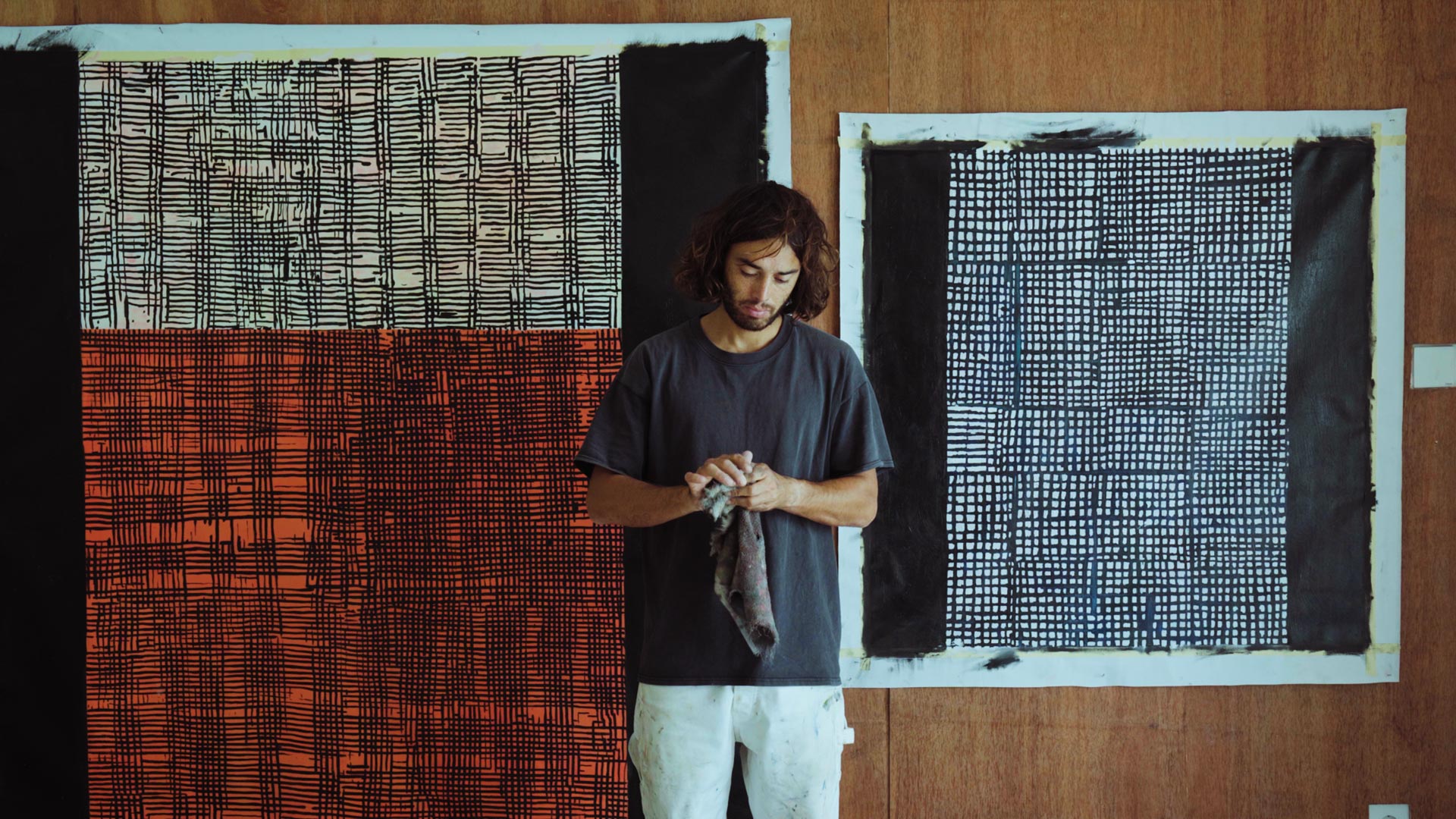 An image of Naleye holding a cloth in his hands standing in front of paintings